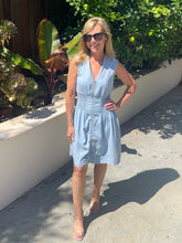 Woman in a light blue dress standing outdoors with plants in the background
