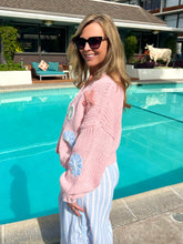 Woman in pink sweater and sunglasses standing by a pool