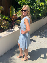 Woman in a light blue dress standing outdoors with greenery in the background