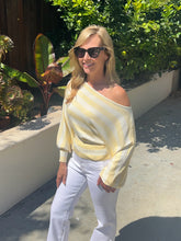 Woman wearing a yellow off-shoulder sweater and white pants standing outdoors.