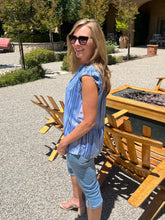 Woman in a blue striped shirt and jeans standing outdoors near wooden chairs.
