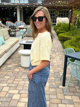 Woman in sunglasses and a yellow top standing on a patio with outdoor furniture.