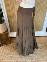 Person wearing a brown tiered skirt with a white top in front of a wall.
