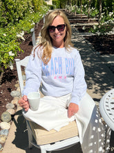 Woman sitting outdoors holding a cup, wearing a 'Beach Bum' sweatshirt