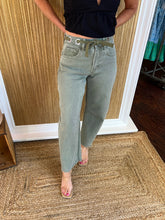 Person wearing light olive barrel jeans and a black top in a store setting.