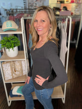 Woman wearing a charcoal long-sleeve top and blue jeans in a store setting.