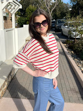 Woman wearing a red and white striped sweater and blue jeans standing outdoors.