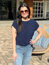 Woman wearing sunglasses and a navy blue top standing outdoors.