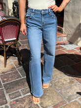 A person wearing light blue high-waisted flare jeans with side stripes, standing on a stone patio.