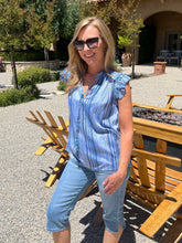 Woman in a blue striped shirt and jeans standing outdoors near wooden benches.