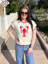 Woman wearing a cream sweater with a red lobster design outdoors.