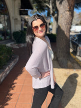Woman wearing sunglasses and a steel blue cardigan on a sidewalk