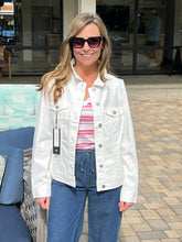 Woman wearing a white jacket, striped shirt, and blue jeans outdoors.