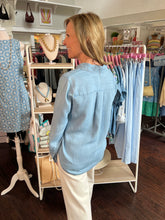 Woman in a denim shirt standing in a clothing store with racks of clothes and mannequins.