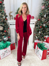 Woman in a red velvet pants standing in a festive room with Christmas trees and decorations.