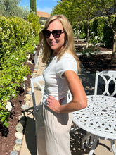Woman in a white dress standing outdoors near a garden and white table.