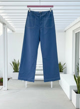 Blue jeans hanging on a white pergola with plants and a white wall in the background