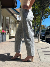 A person standing on a city sidewalk wearing light gray wide-leg jeans with a darker gray animal print pattern, paired with beige block-heel mules.