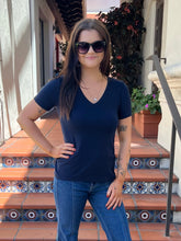 A woman wearing a navy blue v-neck t-shirt and blue jeans stands on tiled outdoor steps, wearing black sunglasses.