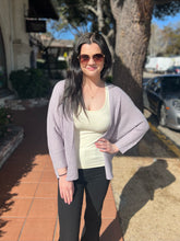 Woman wearing sunglasses and a steel blue cardigan standing on a sidewalk.
