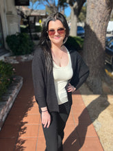 Woman wearing sunglasses and a black cardigan standing outdoors on a sunny day.