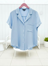 Light blue shirt sleeve solid shirt on a hanger against a white wooden panel background