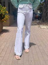 Person wearing white flared jeans and a light green sweater on a sidewalk.