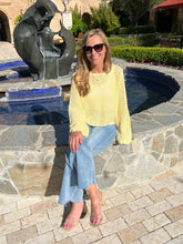 Woman in a yellow sweater and blue jeans sitting by a pool with a sculpture in the background