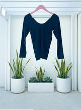 Black long-sleeve shirt on a pink hanger with potted plants in the foreground.