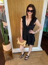 Woman in a black dress standing in front of a wall with a cactus plant nearby.