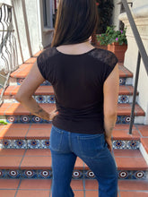 A woman wearing a dark brown cowl-neck sleeveless top and blue jeans, standing on tiled outdoor stairs