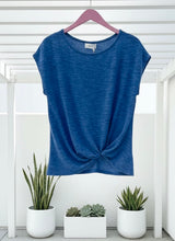 Blue sleeveless top on a hanger with plants in the background
