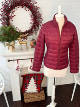 Maroon puffer jacket on a mannequin in front of a Christmas decorated fireplace.