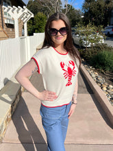 Woman wearing a cream sweater with a red lobster design outdoors.