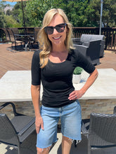 Woman wearing sunglasses and a black top with denim shorts standing outdoors.