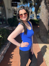 Woman in a blue tank top and sunglasses standing outdoors on a sunny day.