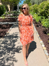 Woman in an orange floral dress walking on a garden path