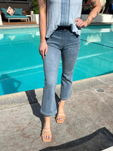 Person wearing a light blue top and jeans standing by a pool.
