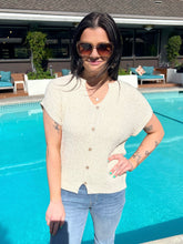 Woman standing by a pool wearing sunglasses and a light-colored shirt.