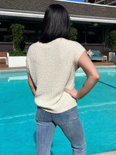 Person wearing a beige textured shirt and blue jeans standing by a pool.