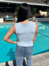 Person wearing a striped tank top and jeans standing by a pool with a cow in the background.