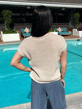 Person standing by a pool wearing a beige sweater and blue pants