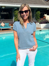 Woman standing by a pool wearing sunglasses and a blue top