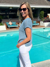 Woman standing by a pool wearing sunglasses and a blue top.