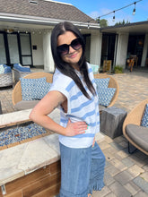 Woman in sunglasses and a striped shirt standing on a patio with outdoor furniture.