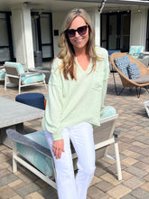Woman in a light green sweater and white pants standing on a patio with outdoor furniture.