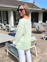 Woman in a light green sweater and sunglasses standing on a patio with outdoor furniture.
