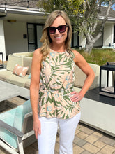 Woman wearing a patterned top and white pants standing outdoors.