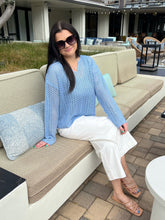 Woman in a blue sweater and white pants sitting on a beige outdoor sofa.