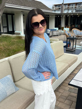 Woman wearing a blue knit sweater and sunglasses in an outdoor setting